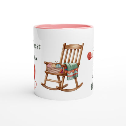 A white ceramic mug with a pink interior, featuring a printed illustration of a wooden rocking chair with a green blanket and a basket of colorful yarn balls, alongside partial text.