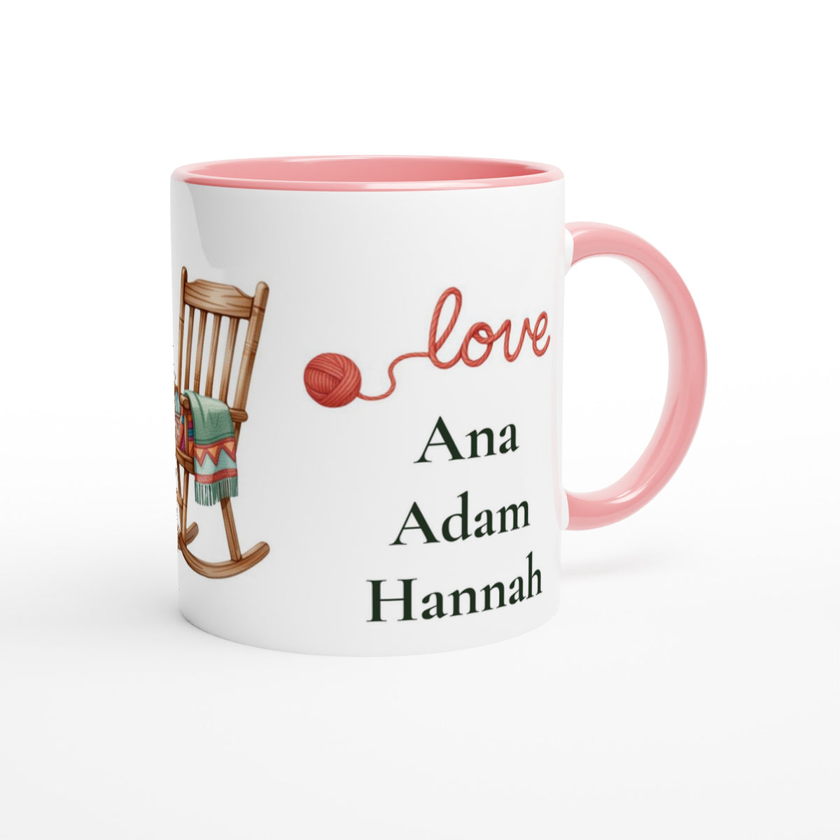 A white ceramic mug with a pink interior and handle, featuring a printed design of a wooden rocking chair with a green blanket, a red ball of yarn, the word 'love' in red script, and the names 'Ana', 'Adam', and 'Hannah' in black text.