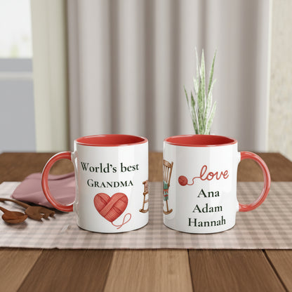 Two personalized ceramic mugs with red interiors and handles, displayed on a wooden table. The mug on the left reads 'World's best GRANDMA' with a red heart-shaped yarn ball graphic.