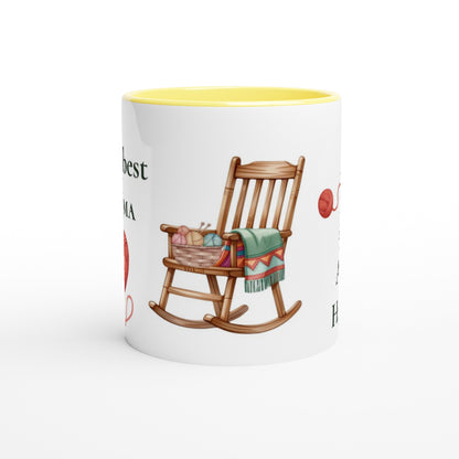 A white ceramic coffee mug with a yellow interior, featuring a printed illustration of a wooden rocking chair with a colorful knit blanket and yarn basket, alongside partial red and black text.