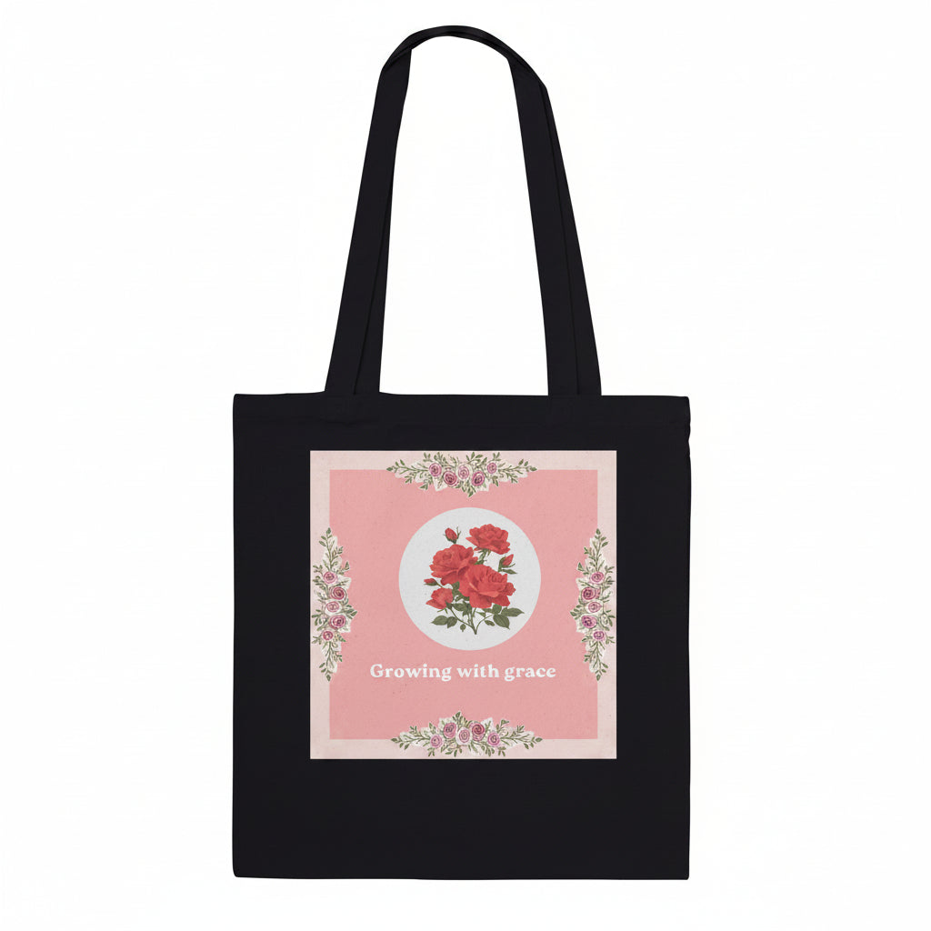 A black canvas tote bag with two shoulder straps, featuring a square pink floral graphic on the front with the text 'Growing with grace'.