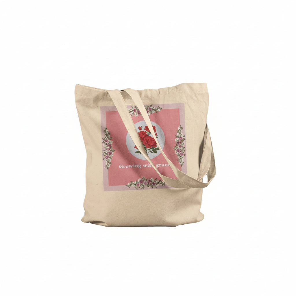 A beige canvas tote bag with dual shoulder straps, featuring a square pink graphic print on the front with a red rose, floral border, and the text 'Growing with grace'.