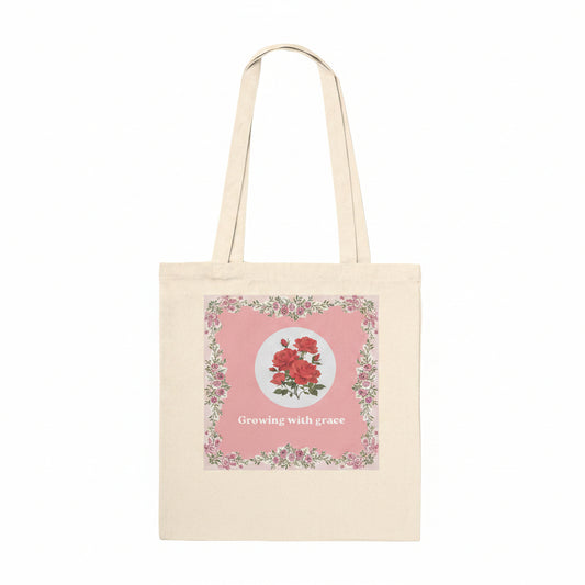 A natural canvas tote bag with a pink floral graphic on the front featuring red roses and the text 'Growing with grace'.