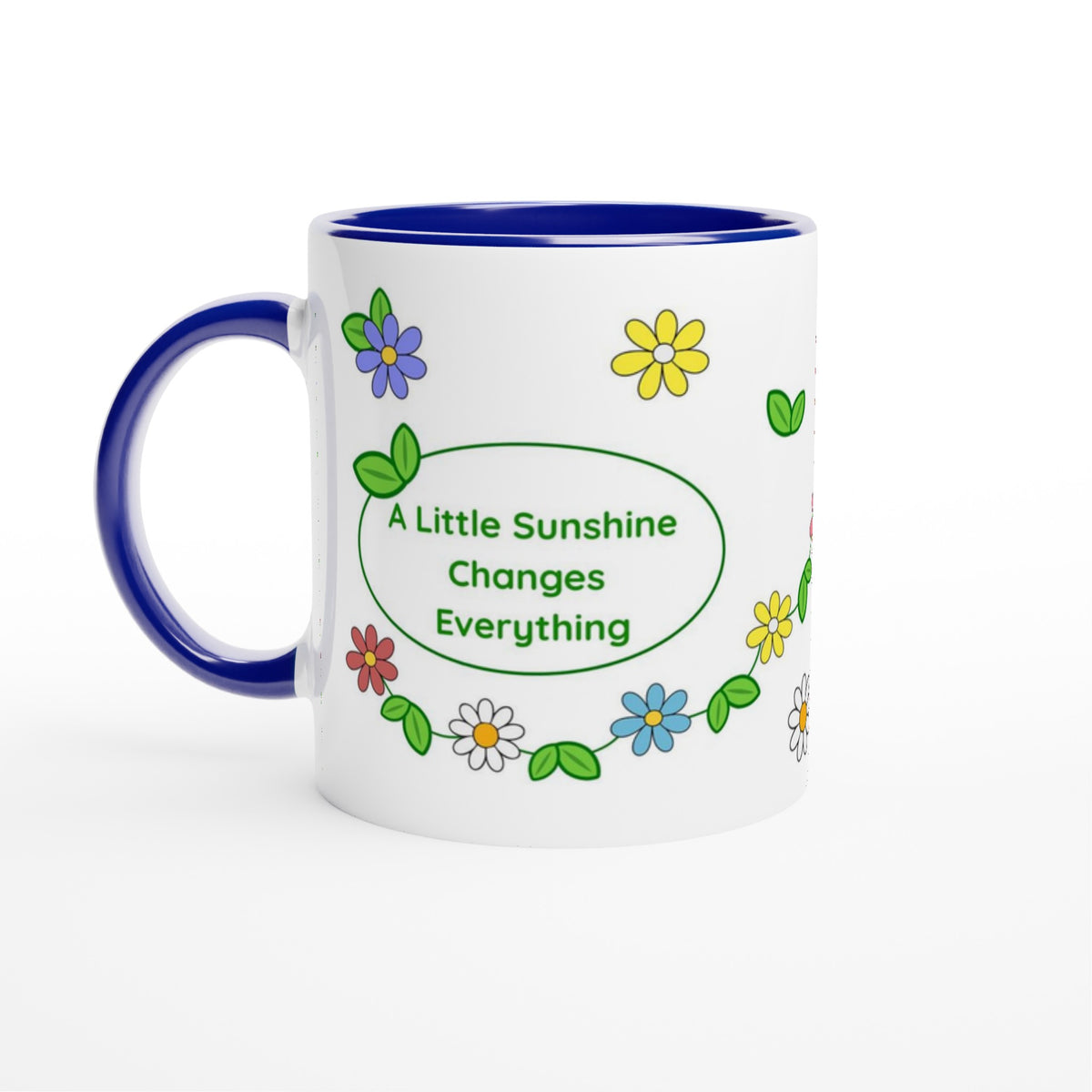 A white ceramic mug with a dark blue handle and interior, decorated with colorful flowers and green leaves around a central green oval that reads 'A Little Sunshine Changes Everything'.