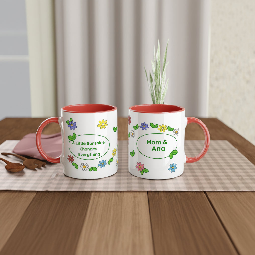 Two white ceramic mugs with coral red interiors and handles, decorated with colorful flowers and personalized text, displayed on a checkered placemat on a wooden table.