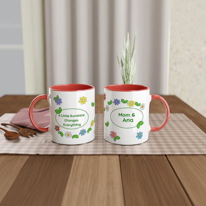 Two white ceramic mugs with coral red interiors and handles, decorated with colorful flowers and personalized text, displayed on a checkered placemat on a wooden table.