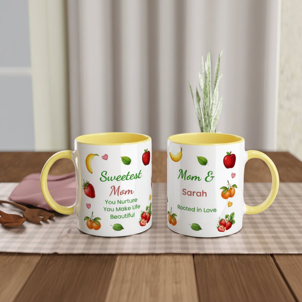 Two white ceramic mugs with yellow interiors and handles, decorated with colorful fruit illustrations and personalized text, displayed on a wooden table with a curtain backdrop.