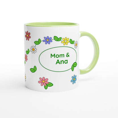 A white ceramic mug with a light green handle and interior, decorated with colorful cartoon flowers and a green oval frame containing the text 'Mom & Ana'.