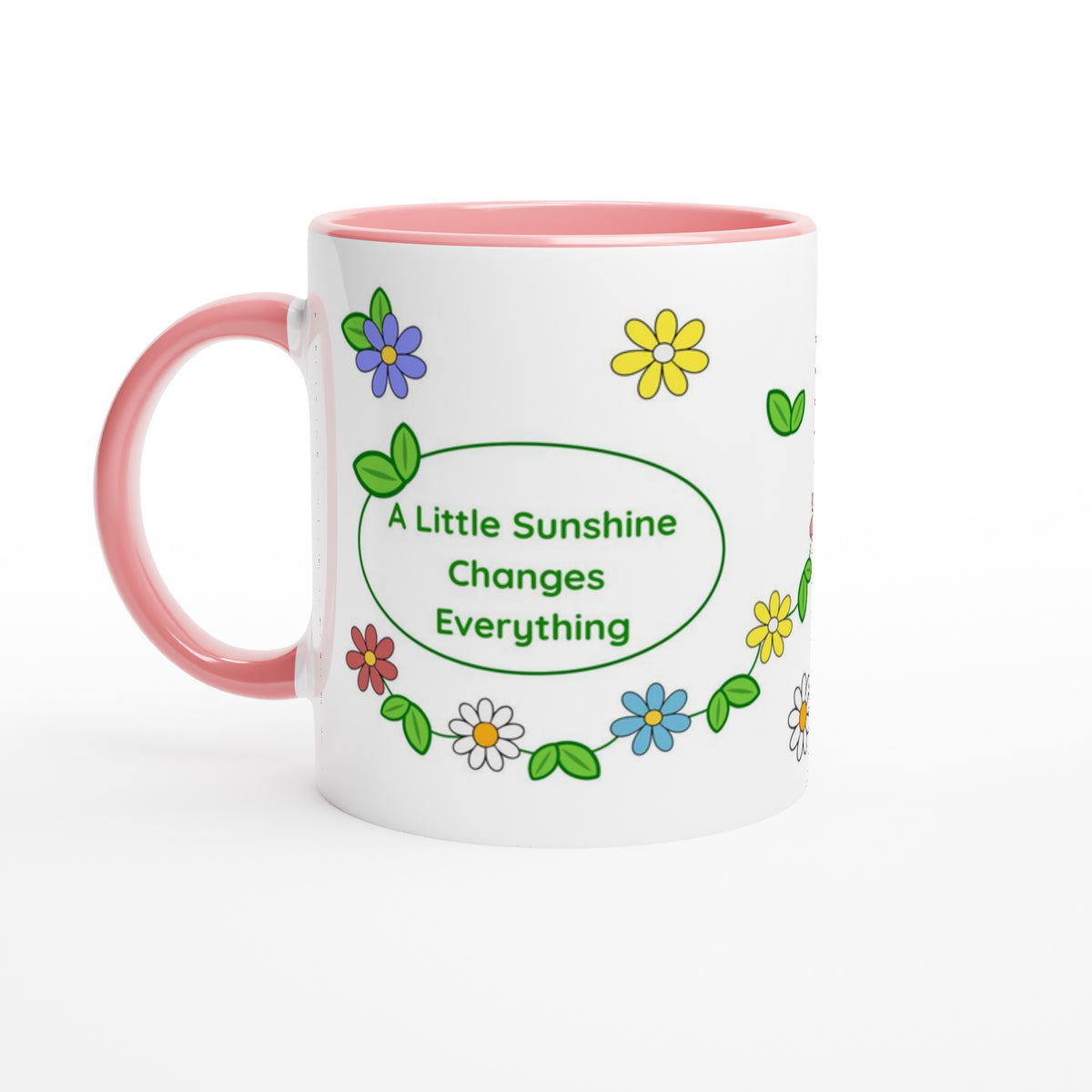 A white ceramic mug with a pink handle and interior, decorated with colorful cartoon flowers and green leaves around a central green oval that reads, 'A Little Sunshine Changes Everything.'.