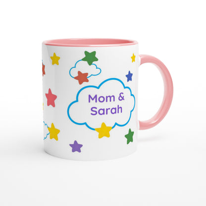 A white ceramic mug with a pink interior and handle, decorated with colorful stars and a blue cloud containing the text 'Mom & Sarah'.