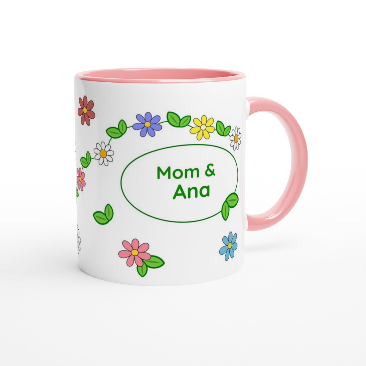 A white ceramic mug with a pink interior and handle, decorated with colorful cartoon flowers and a green oval frame containing the text 'Mom & Ana'.