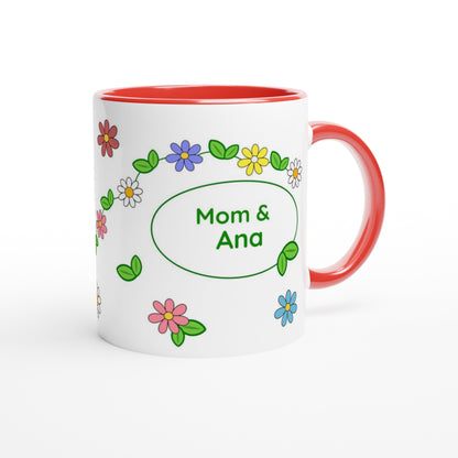 A white ceramic mug with a red interior and red handle, decorated with colorful cartoon flowers and green leaves around a green oval that reads 'Mom & Ana'.