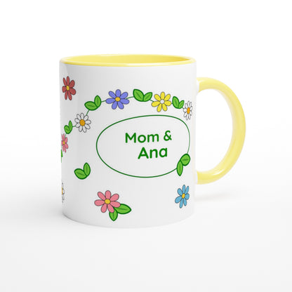 A white ceramic mug with a yellow interior and handle, decorated with colorful cartoon flowers and green leaves around a central oval that reads 'Mom & Ana'.