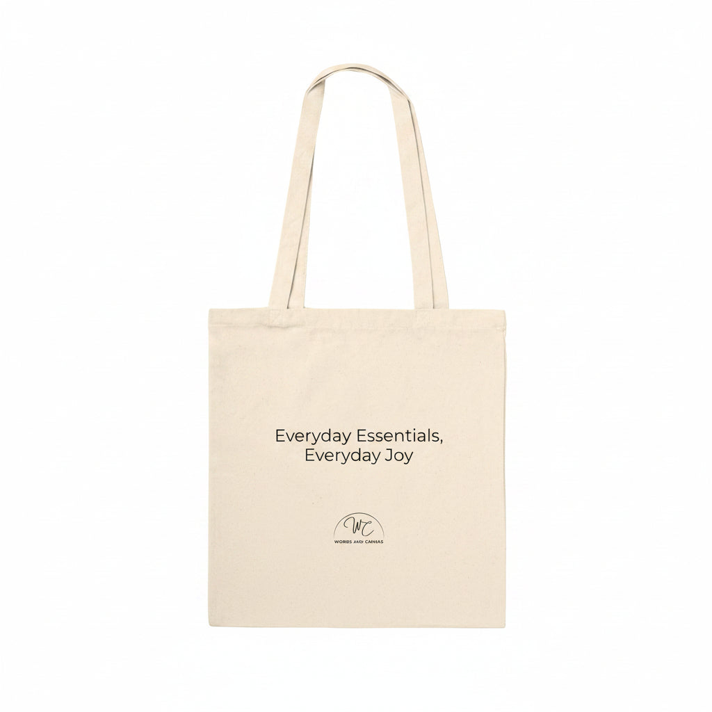 A natural beige canvas tote bag with black printed text reading 'Everyday Essentials, Everyday Joy' and a small circular logo below, shown on a plain white background.