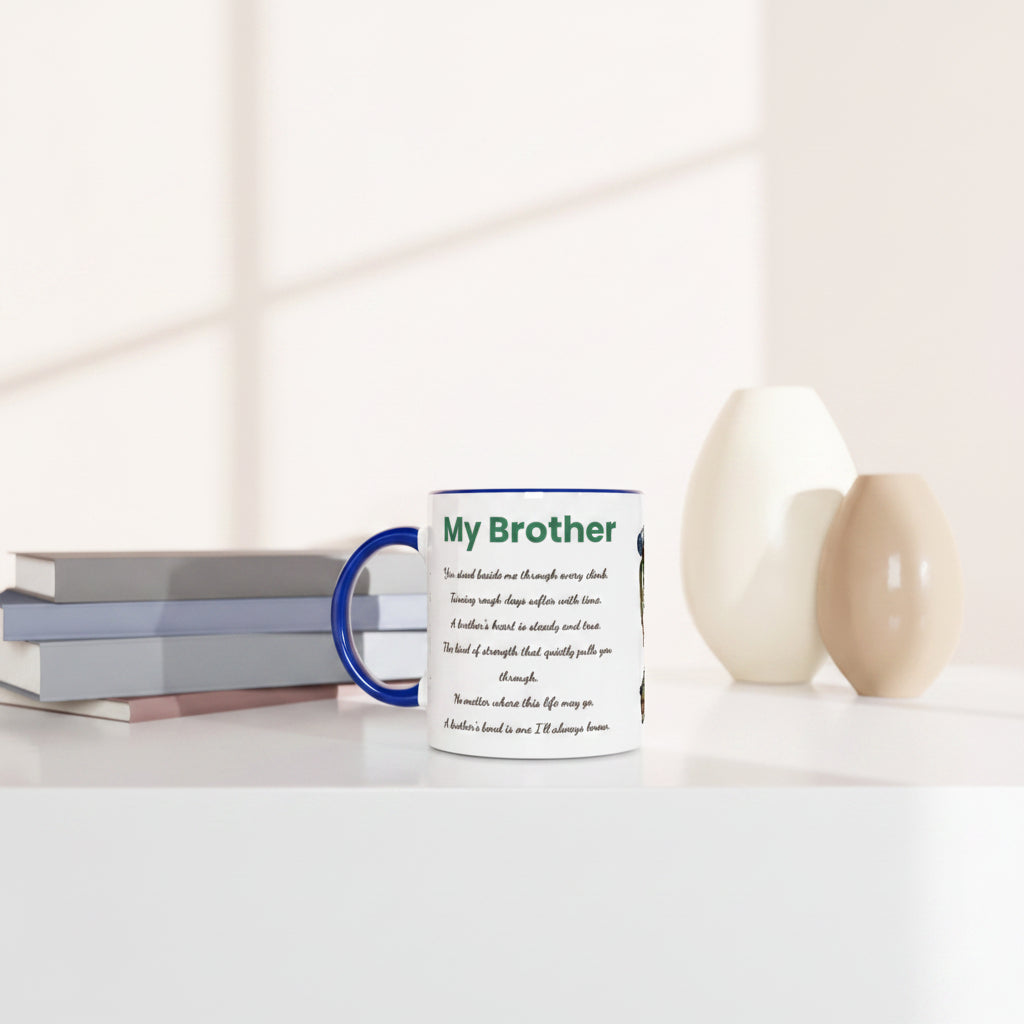 A white ceramic mug with a blue handle and rim sits on a white tabletop beside stacked books and two matte vases. The mug has green and black text reading 'My Brother' with a short poem underneath.