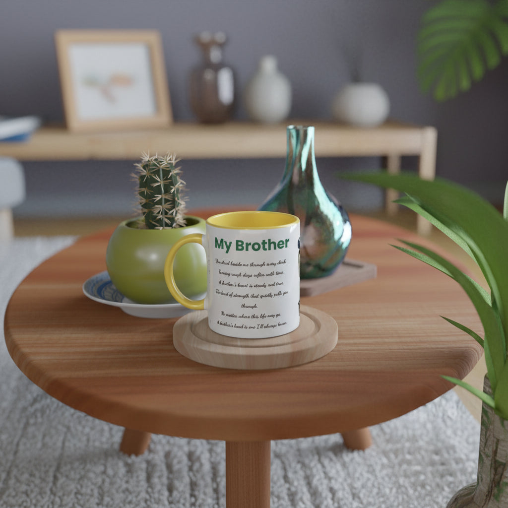 A white ceramic mug with a yellow handle and rim sits on a wooden coaster on a round wooden table. The mug features a humorous printed poem titled 'My Brother'.