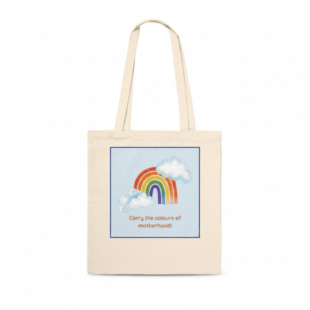 A natural canvas tote bag with a printed graphic of a rainbow and clouds on a light blue background, with the text 'Carry the colours of motherhood!' in orange, shown on a plain white background.