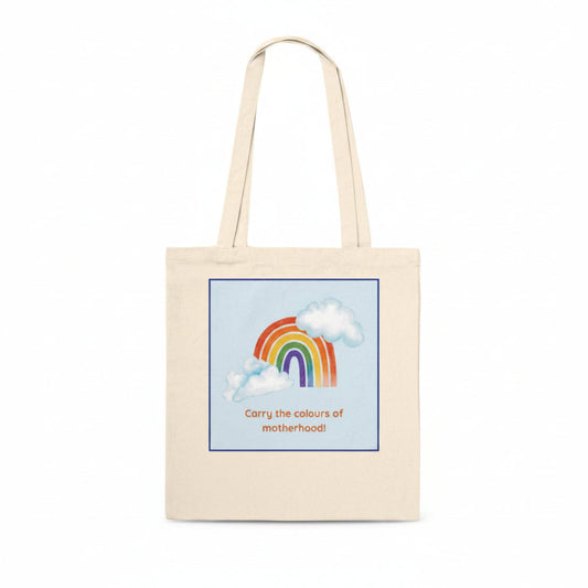A natural canvas tote bag with a printed graphic of a rainbow and clouds on a light blue background, with the text 'Carry the colours of motherhood!' in orange, shown on a plain white background.