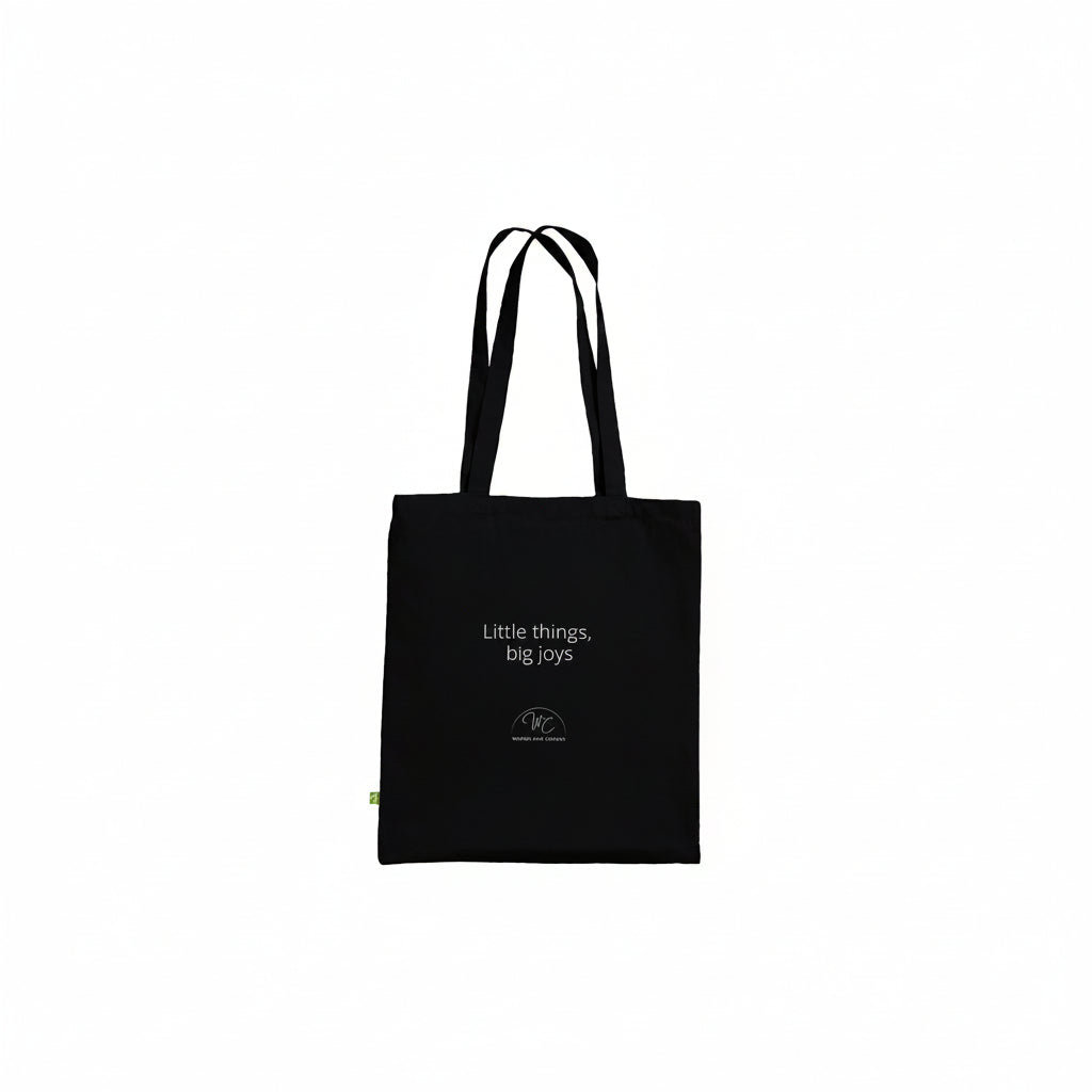 A black canvas tote bag with white printed text reading 'Little things, big joys' and a small circular logo near the bottom, shown against a plain white background.