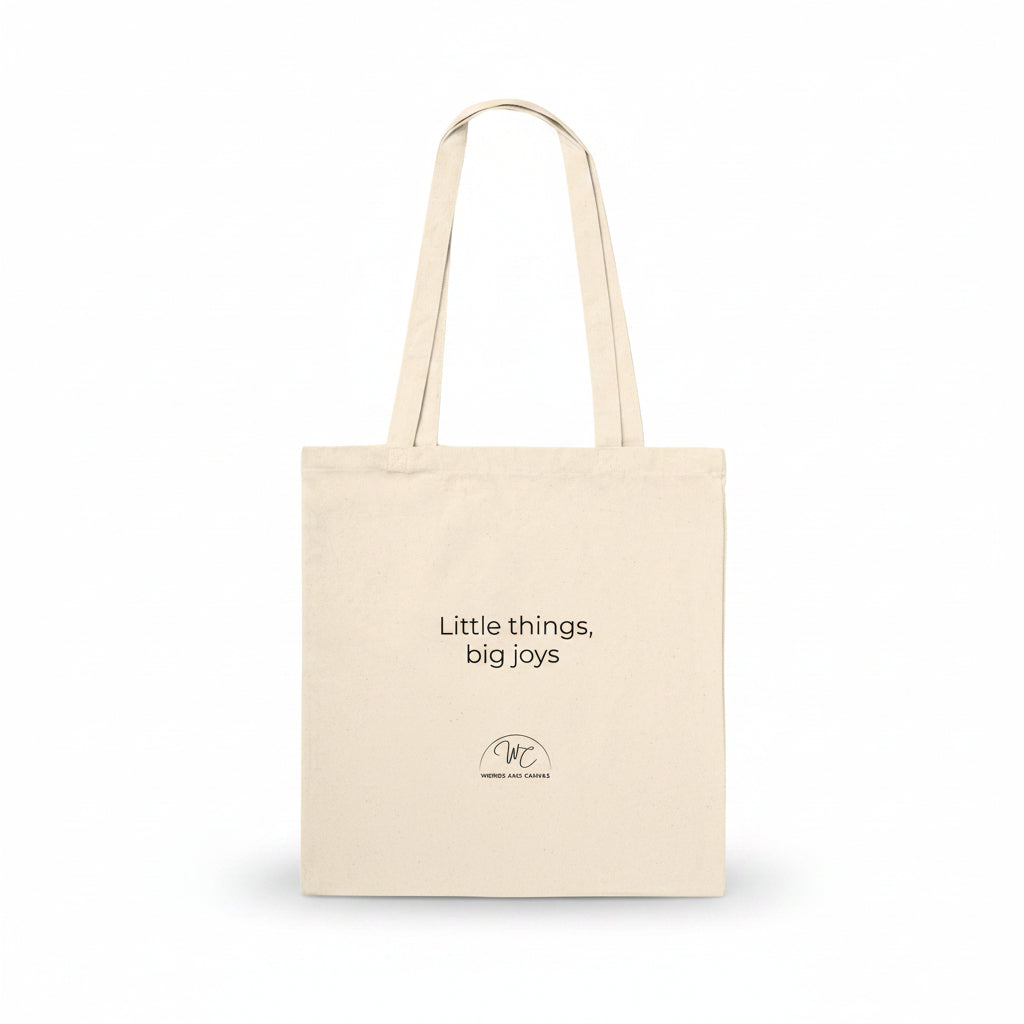 A natural canvas tote bag with black printed text reading 'Little things, big joys' and a small circular logo below, shown on a clean white background.