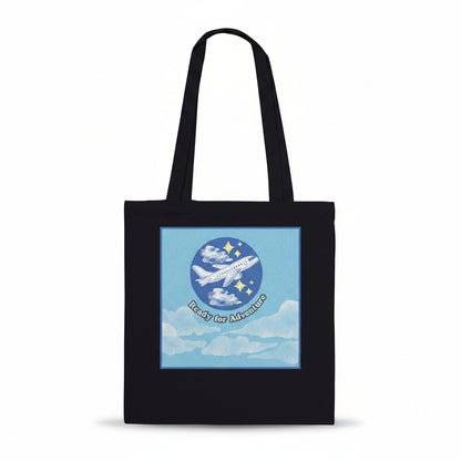 A black canvas tote bag with two shoulder straps, featuring a square graphic print on the front. The graphic shows a light blue sky with white clouds, a white airplane