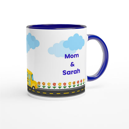 A white ceramic mug with a dark blue handle and interior, decorated with a cartoon school bus, flowers, a road, and the text 'Mom & Sarah' in blue, shown on a white background.