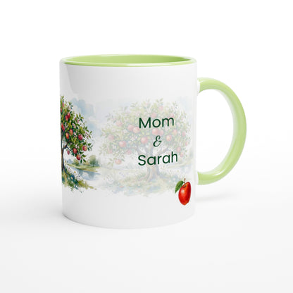 A white ceramic mug with a light green interior and handle, featuring a printed watercolor design of an apple tree and the personalized text 'Mom & Sarah' on the front.