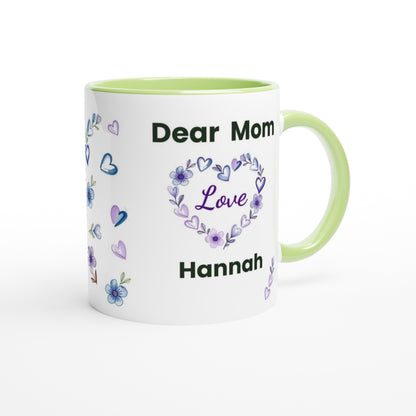 A white ceramic mug with a light green handle and interior, printed with the text 'Dear Mom Love Hannah' in black and purple, surrounded by small purple and blue flowers and hearts.