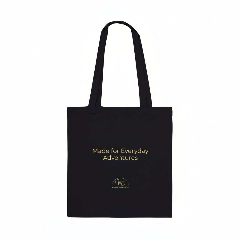 A black canvas tote bag with two shoulder straps, featuring the text 'Made for Everyday Adventures' in yellow on the front, along with a small circular logo below it, set against a plain white background.