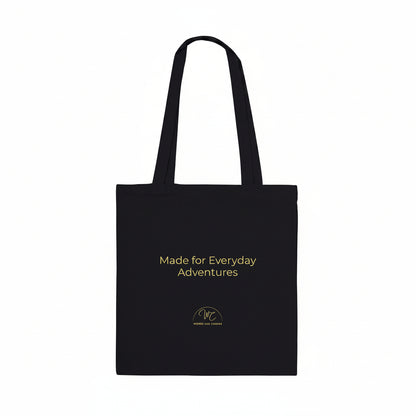 A black canvas tote bag with two shoulder straps, featuring the text 'Made for Everyday Adventures' in yellow on the front, along with a small circular logo below it, set against a plain white background.
