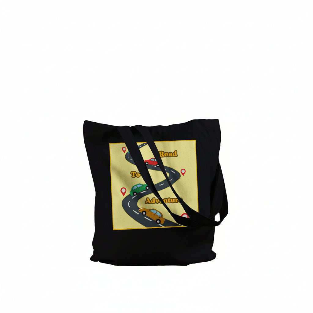 A black canvas tote bag with black shoulder straps, featuring a graphic print on the front. The print shows a winding road with cartoon cars and the words 'Road to Adventure' on a pale yellow background.