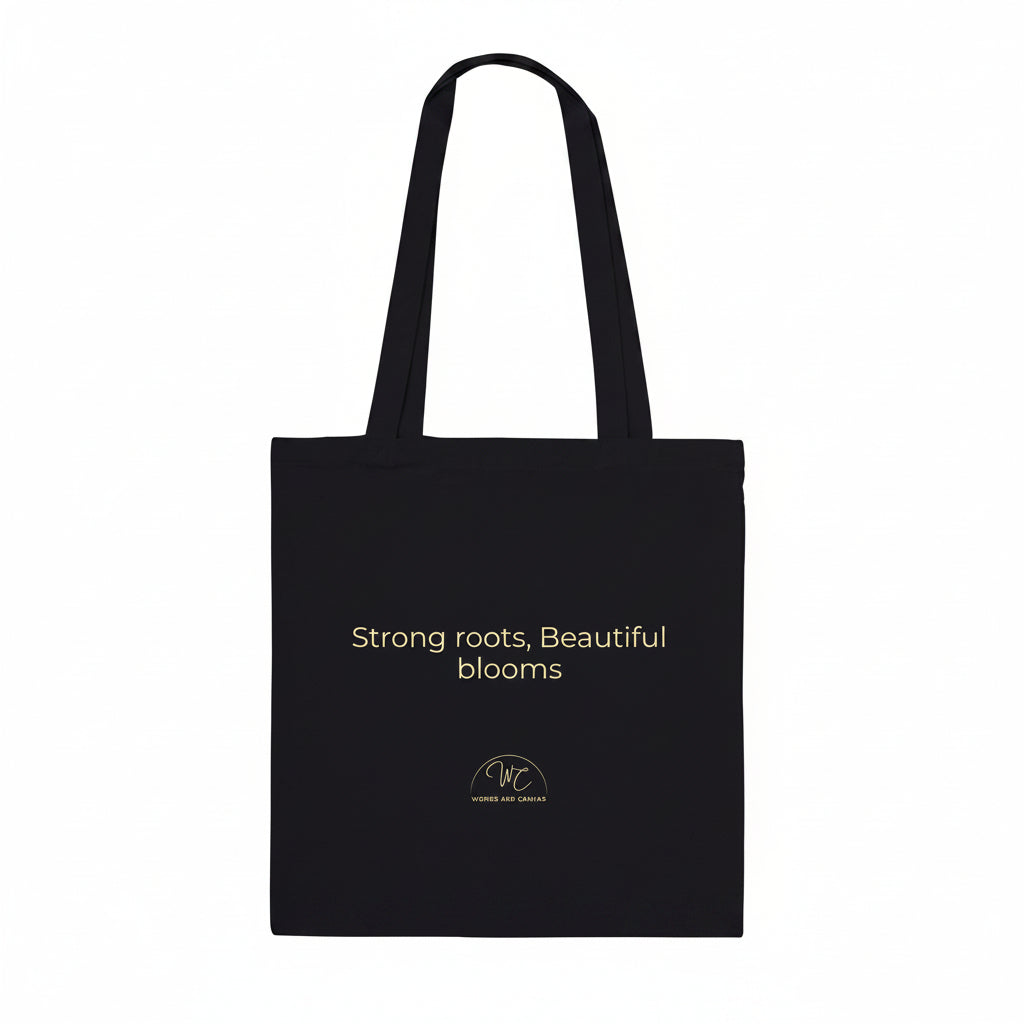 A black canvas tote bag with two shoulder straps, featuring the text 'Strong roots, Beautiful blooms' 