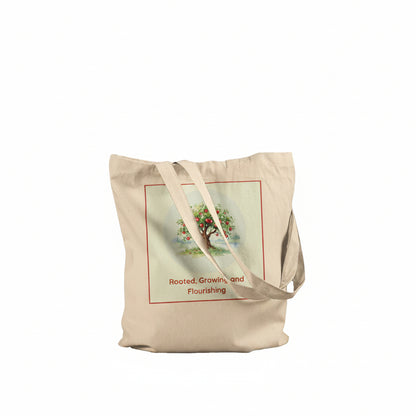 A beige canvas tote bag with two shoulder straps, featuring a vintage-style illustration of an apple tree with the text 'Rooted, Growing, and Flourishing' printed on the front.