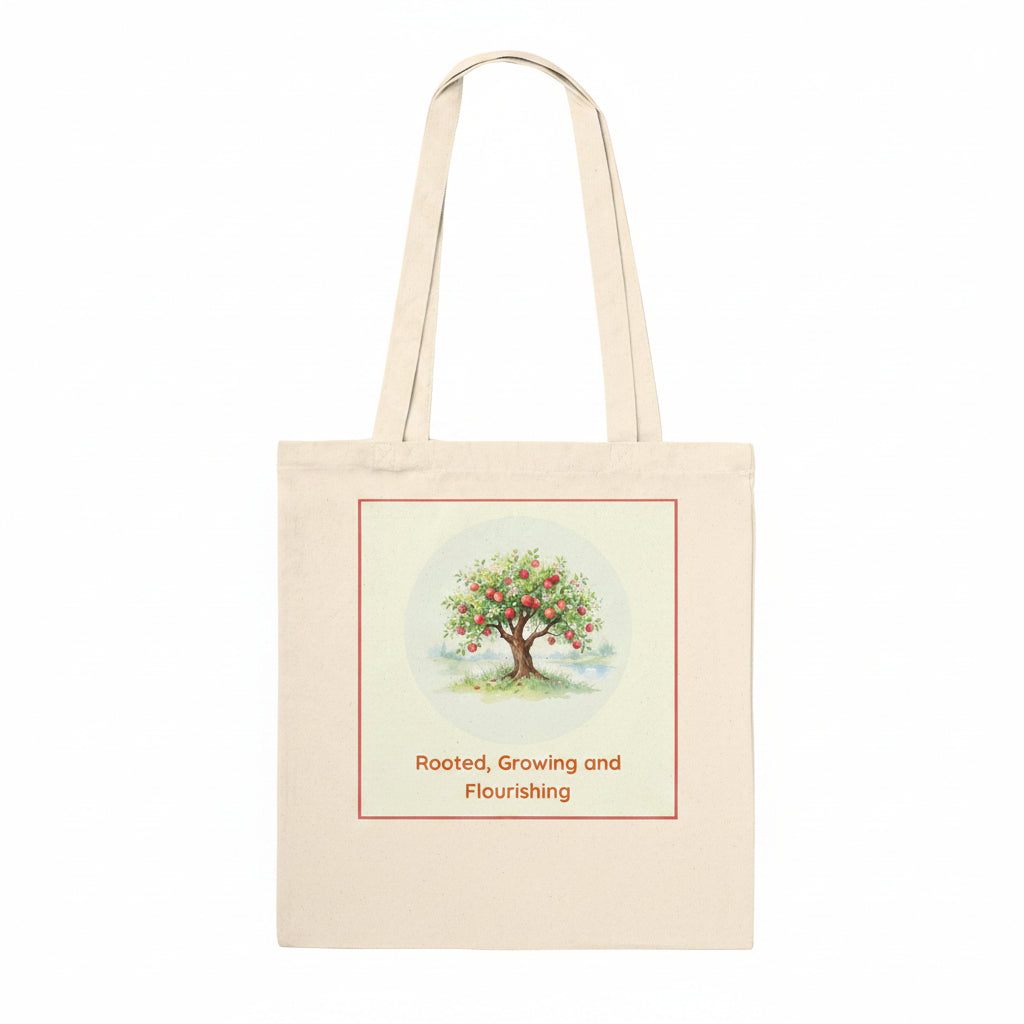 A natural canvas tote bag with two shoulder straps, featuring a printed graphic of a fruit tree with red apples and the text 'Rooted, Growing and Flourishing' on the front.