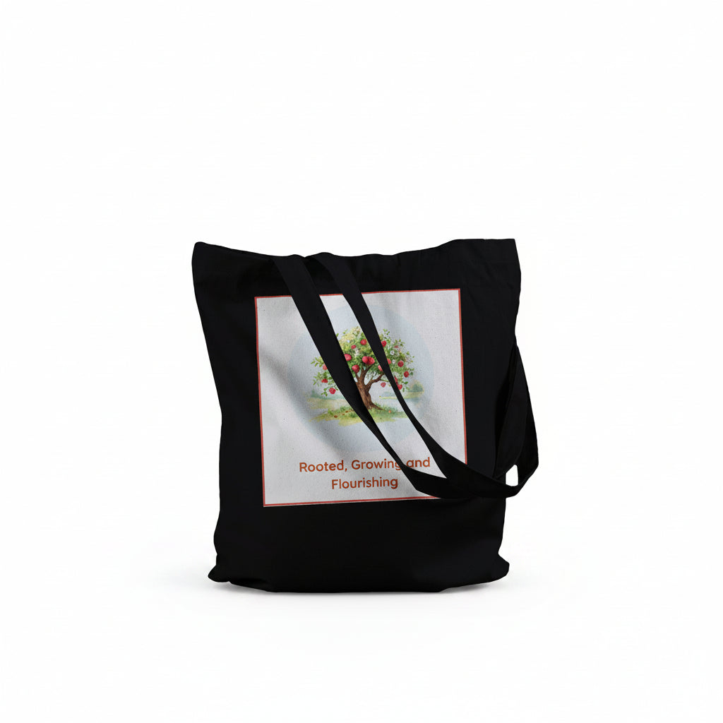 A black canvas tote bag with black shoulder straps, featuring a square graphic print on the front. The print shows a stylized tree with green and orange leaves 