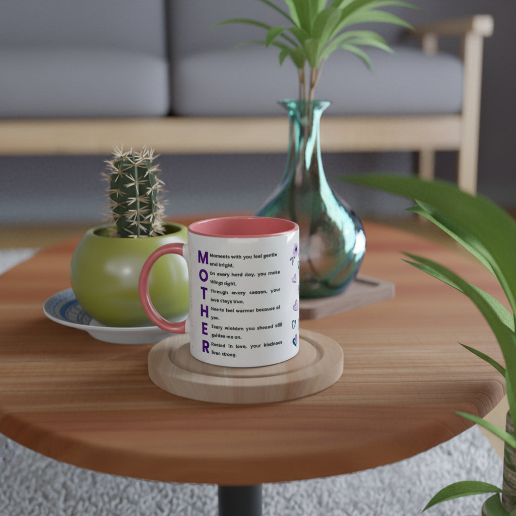 A white ceramic mug with a pink interior and purple text spelling 'MOTHER' sits on a round wooden coaster on a round wooden table. The mug is styled in a cozy living room setting with a small potted cactus, a green vase, and a gray sofa in the background.