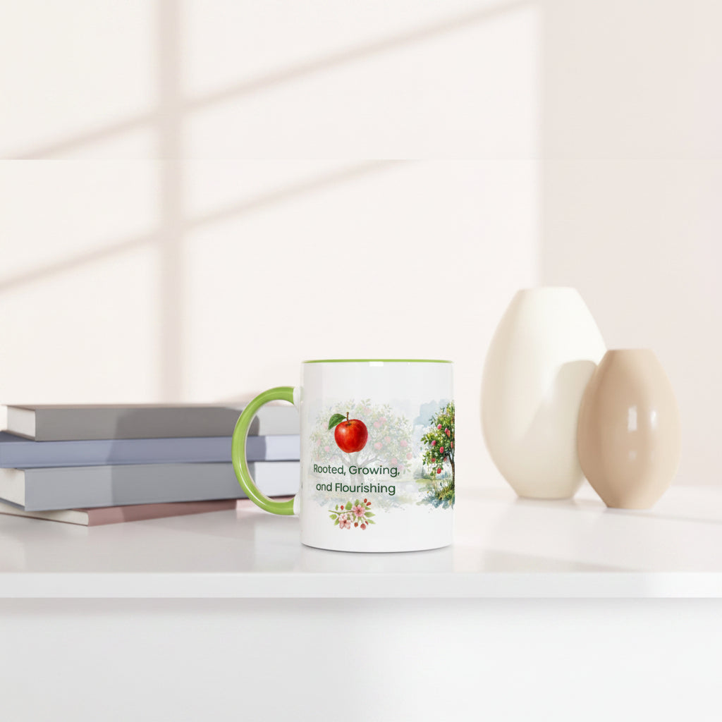 A white ceramic mug with a green handle and green rim, featuring a red apple illustration and the words 'Best Growing and Flourishing' on a white surface next to stacked books and two ceramic vases.