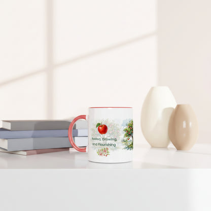 A white ceramic mug with a pink handle and rim sits on a white tabletop beside stacked books and two matte vases.
