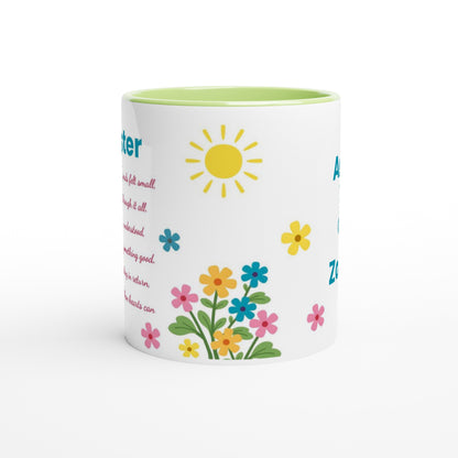 A white ceramic coffee mug with a light green interior, decorated with a yellow sun, colorful flowers, and partial blue and pink text on a white background.