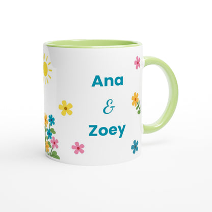 A white ceramic mug with a light green handle and interior, decorated with colorful flowers and the personalized names 'Ana & Zoey' in teal text.