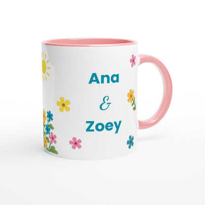 A white ceramic mug with a pink interior and handle, decorated with colorful flowers and the names 'Ana & Zoey' in blue text, on a white background.