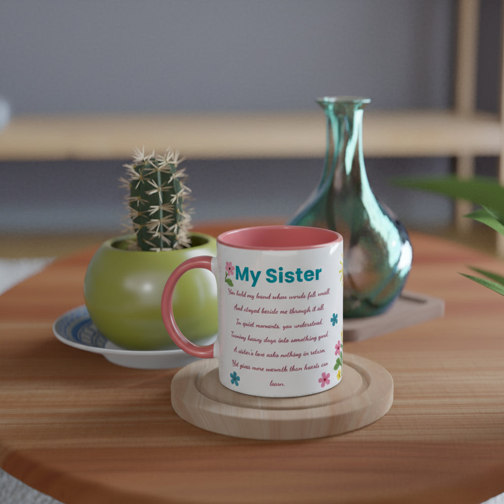 A white ceramic mug with a pink interior and handle, printed with a poem titled 'My Sister' and small colorful flowers, sitting on a wooden coaster on a wooden table. A small potted cactus and a green glass vase are in the background.