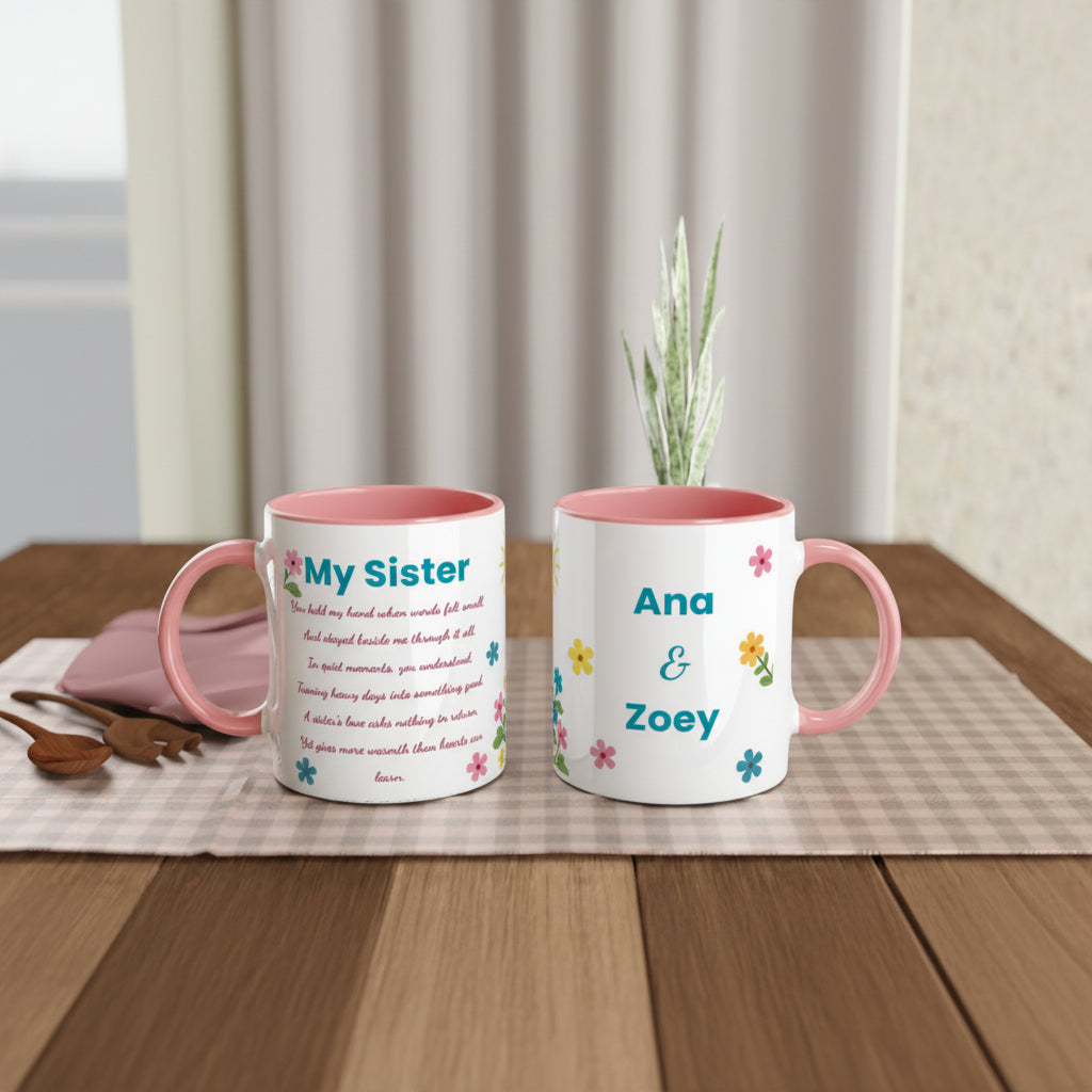 Two personalized ceramic mugs with pink interiors and handles, displayed on a wooden table with a checkered runner, a small plant, and a pink plate in the background. One mug reads 'My Sister' with printed text, and the other reads 'Ana & Zoey' with small colorful flowers.