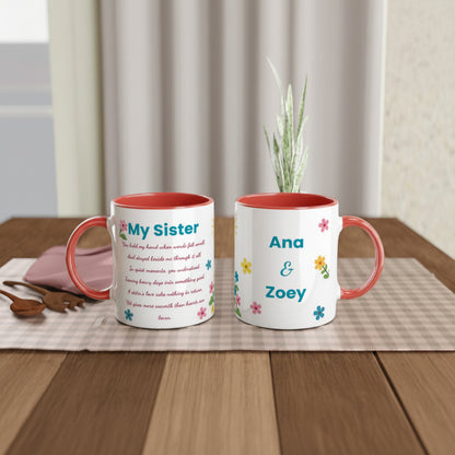 Two personalized ceramic mugs with coral-red interiors and handles, displayed on a wooden table. One mug features a poem titled 'My Sister' in black text with small multicolor flower accents, and the other features the names 'Ana & Zoey' in teal with matching flowers.