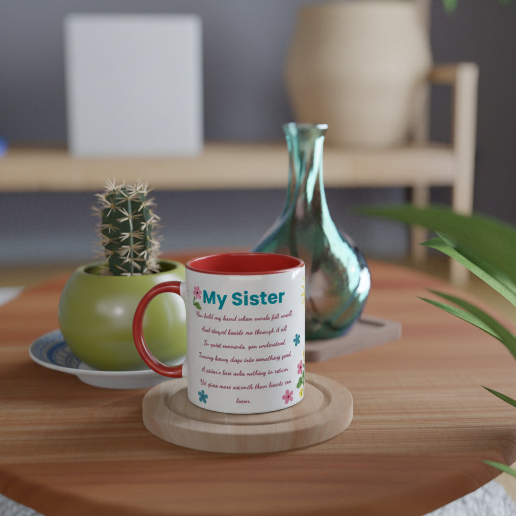 A white ceramic mug with a red handle and interior, printed with a poem titled 'My Sister' in blue and pink text, displayed on a wooden coaster on a round wooden table. The background features a green potted cactus and a decorative teal glass vase.
