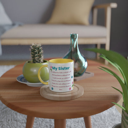 A white ceramic mug with a yellow interior and handle, printed with the text 'My sister' and a poem, sitting on a wooden coaster on a round wooden table in a cozy living room setting.