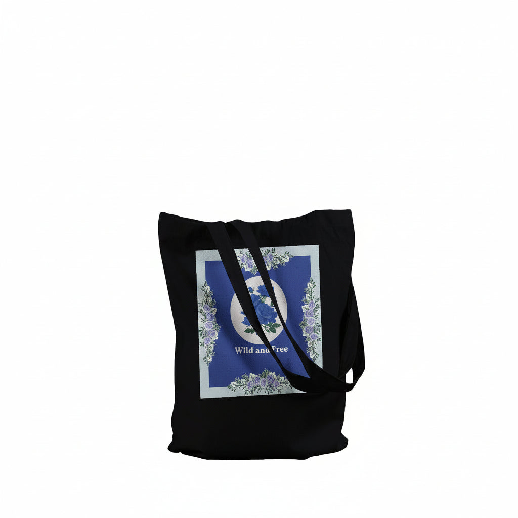 A black canvas tote bag with a large square graphic print on the front. The print features a blue background with a white circular emblem, floral details, and the words 'Wild and Free'.