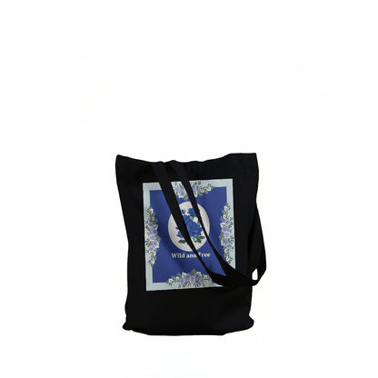 A black canvas tote bag with a large square graphic print on the front. The print features a blue background with a white circular emblem, floral details, and the words 'Wild and Free'.
