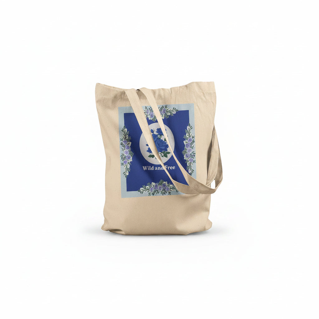 A natural canvas tote bag with a blue and white floral graphic on the front, featuring the words 'Wild and Free' and long shoulder straps, set against a plain white background.