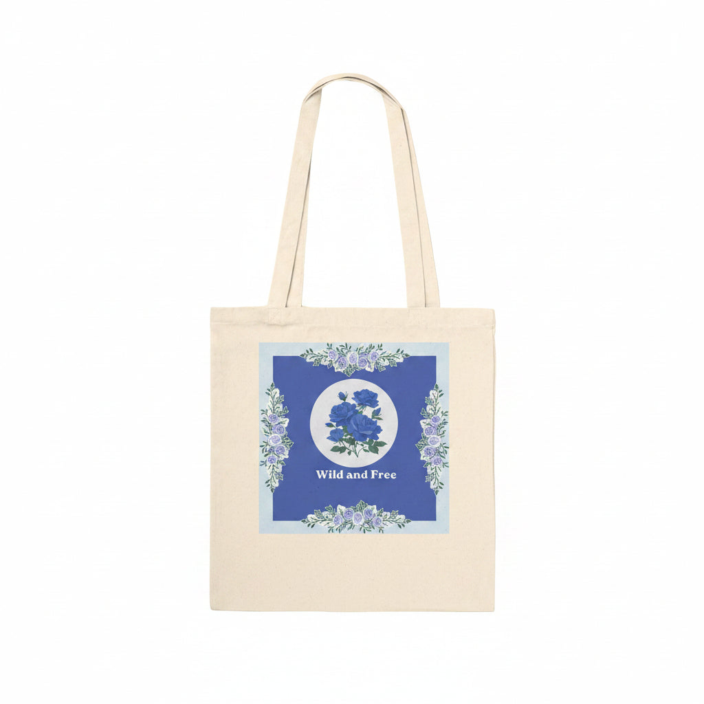 A natural canvas tote bag with a blue and white floral graphic on the front, featuring the text 'Wild and Free' and two shoulder straps, shown against a plain white background.
